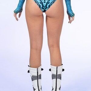 May include: High-waisted bikini bottoms featuring a vibrant blue and black butterfly wing pattern with side cutouts, paired with matching long-sleeved arm sleeves and white mid-calf platform boots with black mesh panels and back zips.