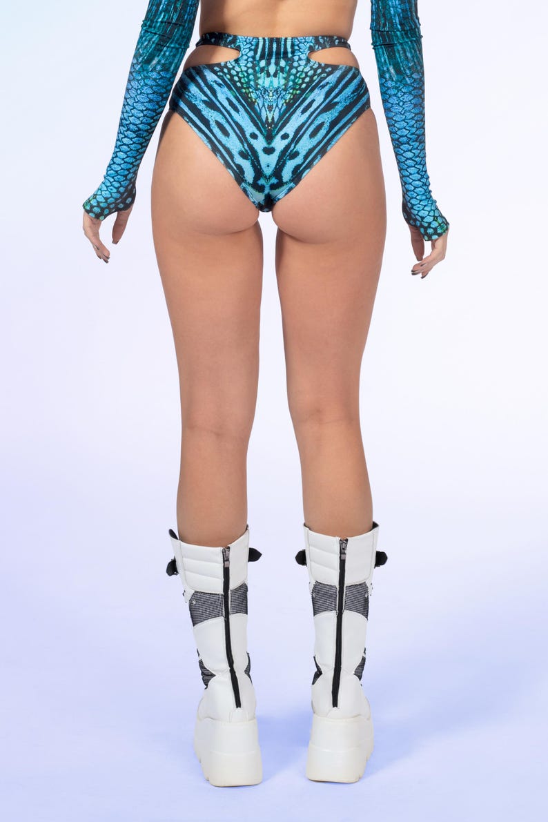 May include: High-waisted bikini bottoms featuring a vibrant blue and black butterfly wing pattern with side cutouts, paired with matching long-sleeved arm sleeves and white mid-calf platform boots with black mesh panels and back zips.
