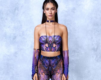 May include: A matching purple and gold patterned crop top, trousers, and arm sleeves. The outfit has a strapless top and is paired with a choker necklace. The outfit is a unique design.