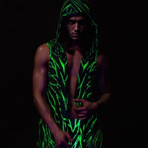 May include: A sleeveless hooded garment featuring a black background with striking neon green vein-like patterns. The open front reveals the chest, and the hood frames the face. The overall aesthetic is dark and edgy, with a focus on the striking colour contrast.