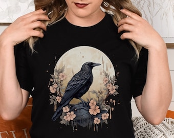 May include: Black t-shirt with a graphic of a crow perched on a rock with flowers and a full moon in the background.