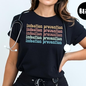 May include: Black t-shirt with the text "infection prevention" in a retro font. A stethoscope is draped around the neck. The shirt is a crew neck style.