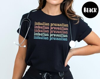 May include: Black t-shirt with the text "infection prevention" in a retro font. A stethoscope is draped around the neck. The shirt is a crew neck style.
