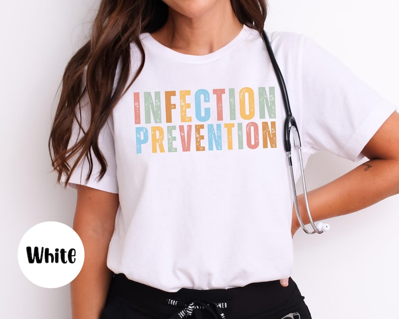 May include: White t-shirt with the words "INFECTION PREVENTION" in colorful, textured letters. A stethoscope hangs around the neck. The shirt is a crew neck style.
