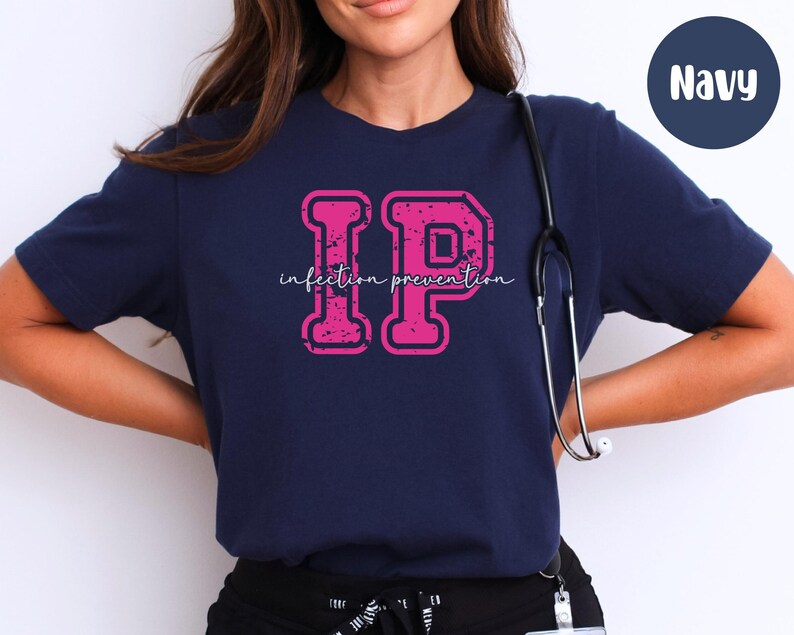 Puede incluir: Camiseta azul marino con las letras "IP" en fuente rosa desgastada, con las palabras "Infection Prevention" en fuente cursiva. Un estetoscopio cuelga alrededor del cuello.
