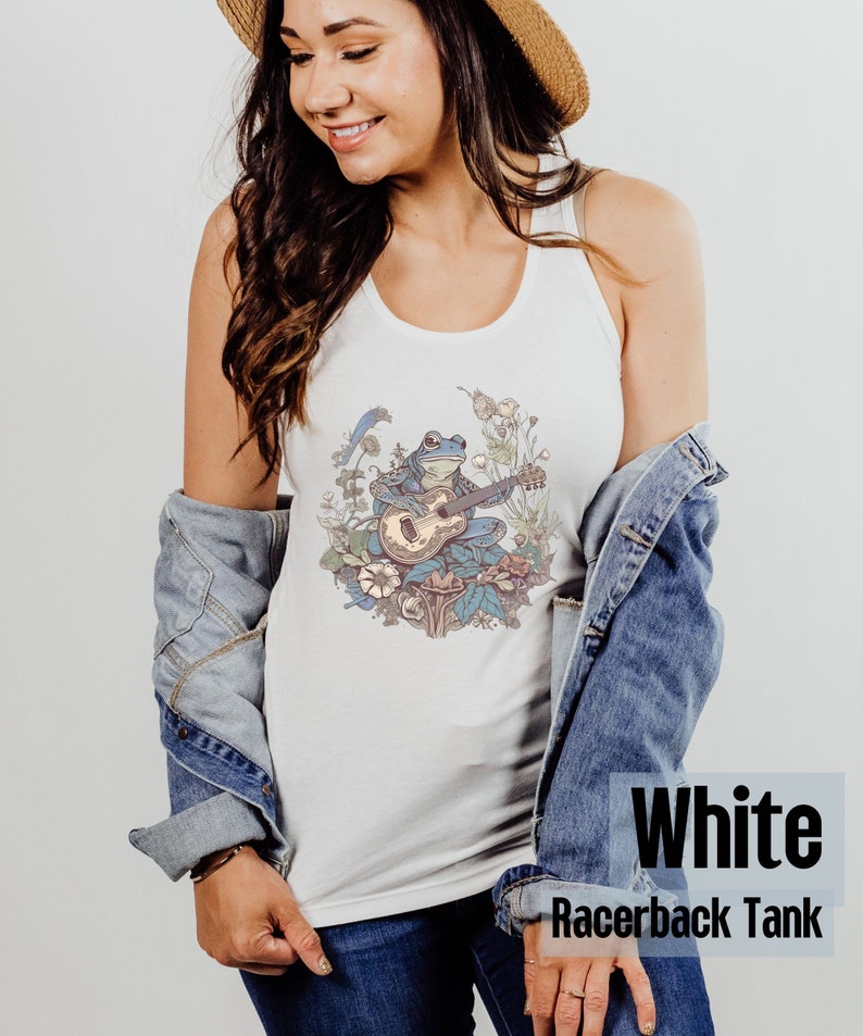 May include: White racerback tank top with a graphic of a frog playing a guitar in a floral setting.