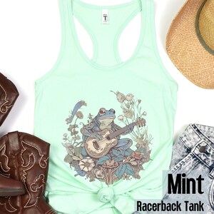 May include: Mint green racerback tank top with a graphic of a frog playing a guitar surrounded by flowers and mushrooms.