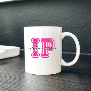 Puede incluir: Taza de cer&aacute;mica blanca con un gran dise&ntilde;o "IP" rosa y las palabras "infection prevention" en una fuente cursiva. Las letras tienen un aspecto texturizado y desgastado. La taza tiene un asa curva y est&aacute; sobre una superficie oscura.