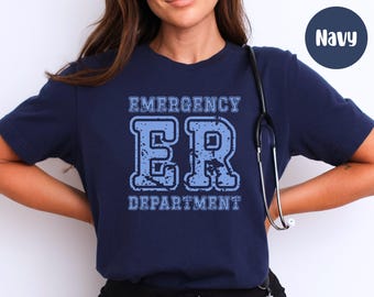 May include: Navy blue t-shirt with the text "EMERGENCY ER DEPARTMENT" in a distressed, light blue collegiate font. A stethoscope hangs on the shirt. The shirt is a solid navy blue color.