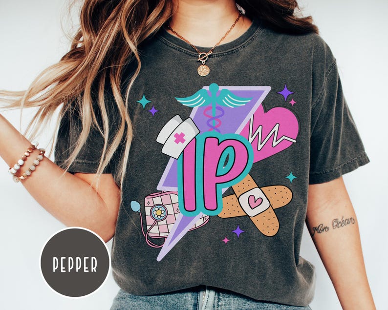 May include: Dark gray t-shirt featuring a colorful graphic design. The design includes a nurse's hat, stethoscope, heart, bandages, and the letters "IP" in a stylized font. The shirt has a vintage, washed look.