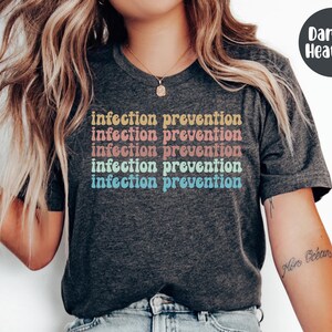 May include: Dark gray heather t-shirt with the words "infection prevention" stacked in a retro font. The text is in a gradient of colors: yellow, pink, orange, blue, and teal. The shirt is a crew neck.