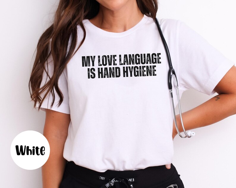 May include: White t-shirt with the text "MY LOVE LANGUAGE IS HAND HYGIENE" in black. A stethoscope hangs around the neck. The shirt is a crew neck style.