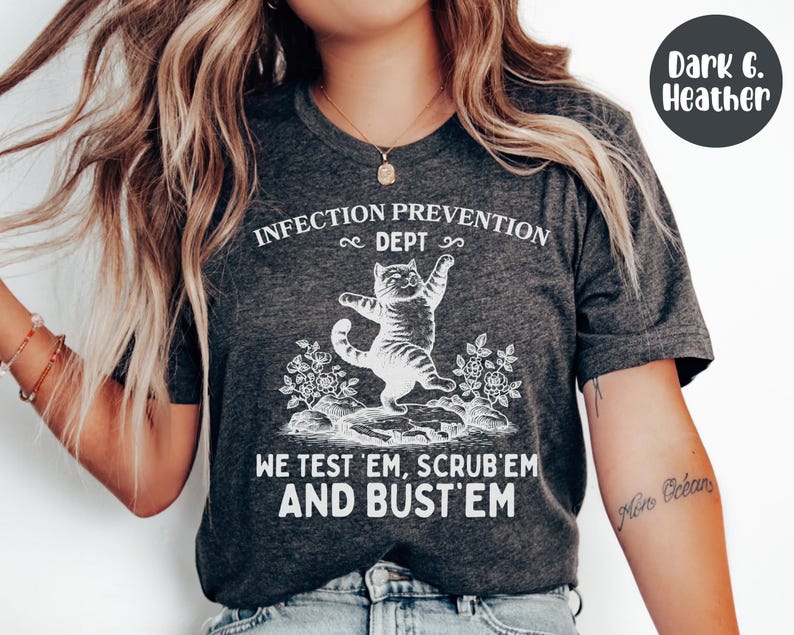 May include: Dark heather gray t-shirt with the text "INFECTION PREVENTION DEPT" and "WE TEST 'EM, SCRUB 'EM AND BUST 'EM". The shirt features a white graphic of a cat standing on its hind legs. The shirt is made of a soft material.