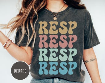 Puede incluir: Camiseta gris oscuro con la palabra "RESP" repetida cuatro veces en diferentes colores: beige, rosa, turquesa y azul. La camiseta tiene un aspecto vintage y desgastado. La palabra "PEPPER" está en un círculo en la parte inferior izquierda.