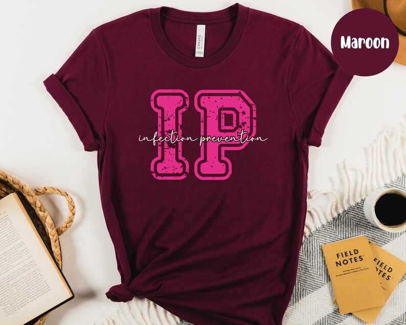 Puede incluir: Camiseta color granate con un gr&aacute;fico "IP" rosa desgastado y la frase "infection prevention" en cursiva. La camiseta es de material suave y tiene las mangas dobladas.