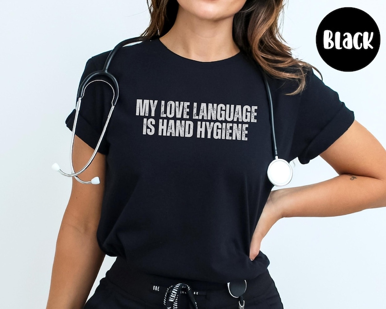 May include: Black t-shirt with the text "MY LOVE LANGUAGE IS HAND HYGIENE" in white, distressed lettering. A stethoscope is draped around the neck. The shirt is a crew neck style.