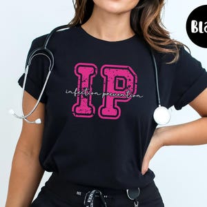 Puede incluir: Camiseta negra con un dise&ntilde;o rosa "IP" desgastado y las palabras "infection prevention". Un estetoscopio cuelga del cuello. Un c&iacute;rculo negro con la palabra "Black" est&aacute; en la esquina superior derecha.
