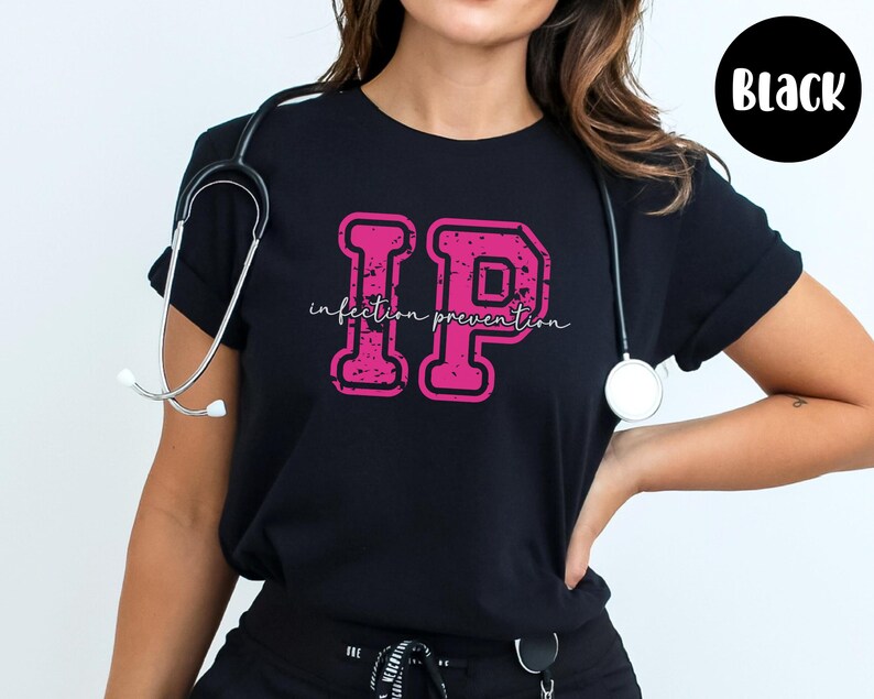 Puede incluir: Camiseta negra con un dise&ntilde;o rosa "IP" desgastado y las palabras "infection prevention". Un estetoscopio cuelga del cuello. Un c&iacute;rculo negro con la palabra "Black" est&aacute; en la esquina superior derecha.