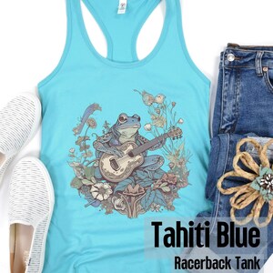 May include: A turquoise blue racerback tank top with a graphic of a frog playing a guitar surrounded by flowers. The text "Tahiti Blue Racerback Tank" is printed on the bottom of the shirt.