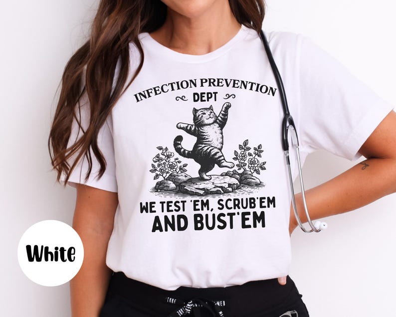 May include: White t-shirt with a black and white graphic of a cat standing on a rock with the text "INFECTION PREVENTION DEPT" and "WE TEST 'EM, SCRUB 'EM AND BUST 'EM". A stethoscope hangs on the shirt.