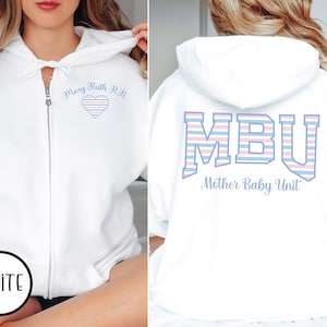 May include: White zip-up hoodie with the text "Mary Ruth R.N." and a heart design on the front. The back of the hoodie features the letters "MBU" and the words "Mother Baby Unit" in a matching font.