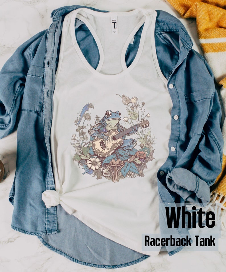 May include: White racerback tank top with a blue frog playing a guitar in a floral setting.
