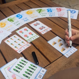 Pu&ograve; includere: Un set di schede educative per contare con numeri, parole scritte e illustrazioni di oggetti come fiori, carote e veicoli. Un pennarello cancellabile bianco viene utilizzato per cerchiare i numeri sulle schede dotate di griglie a dieci.