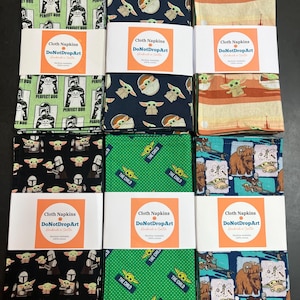 Puede incluir: Un conjunto de servilletas de tela con varios dise&ntilde;os, incluyendo personajes de una popular serie de ciencia ficci&oacute;n. Las servilletas est&aacute;n empaquetadas y etiquetadas con el texto "Cloth Napkins DoNotDropArt".