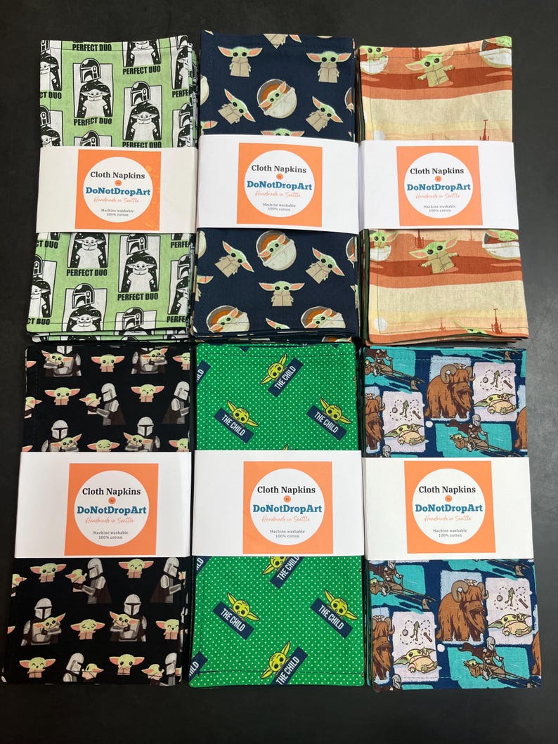 Puede incluir: Un conjunto de servilletas de tela con varios dise&ntilde;os, incluyendo personajes de una popular serie de ciencia ficci&oacute;n. Las servilletas est&aacute;n empaquetadas y etiquetadas con el texto "Cloth Napkins DoNotDropArt".