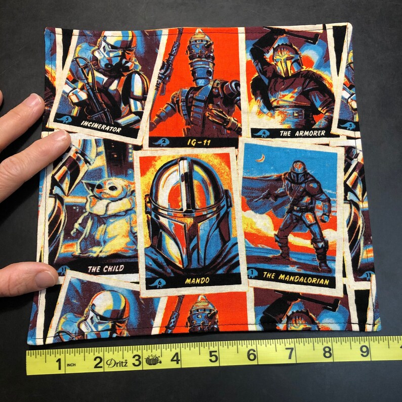 Puede incluir: Un art&iacute;culo de tela cuadrada con un collage de personajes de Star Wars al estilo c&oacute;mic. Los personajes incluyen a The Mandalorian, The Child e IG-11. El art&iacute;culo mide aproximadamente 23 cm de ancho.