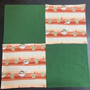 Puede incluir: Cuatro servilletas cuadradas de tela. Dos son de color verde liso y dos presentan un patr&oacute;n repetido de un personaje de dibujos animados en un cuenco blanco, sobre un fondo a rayas naranja, blanco y beige.