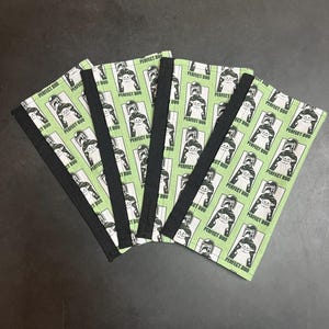 Puede incluir: Cinco art&iacute;culos de tela verde con un patr&oacute;n repetido de un personaje y el texto "PERFECT DUO" en blanco. Cada art&iacute;culo tiene un borde negro. Los art&iacute;culos est&aacute;n abanicados sobre una superficie oscura.