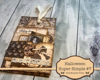 May include: A handcrafted Halloween-themed paper craft with layered pockets and tags. The design features vintage-style patterns, lace trim, and a decorative paper clip. Text includes "It's the witching hour" and "Halloween Super Simple #7".