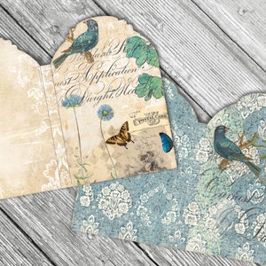 May include: A vintage-style card with a blue bird, butterfly, and floral design. The card is folded in half and has a blue and white patterned background.