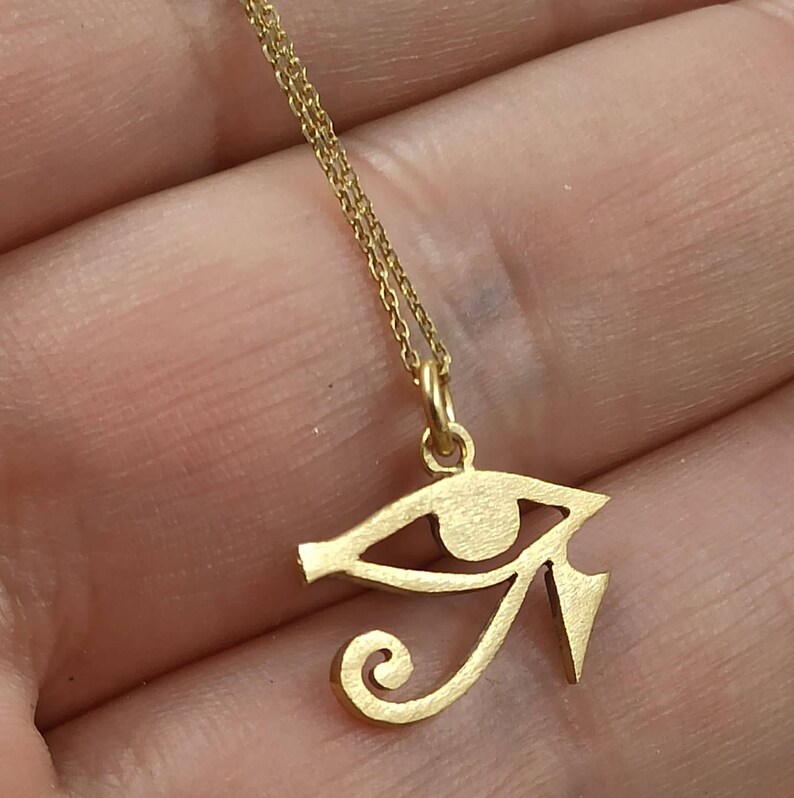 May include: Gold chain necklace with a gold pendant in the shape of the Eye of Horus.