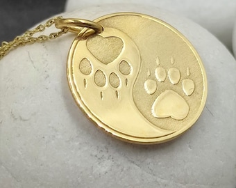 May include: Gold necklace with a pendant featuring a yin yang design with a paw print on each side. One paw print has a heart in the center.