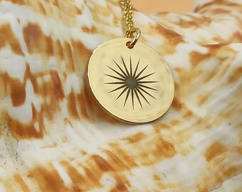 May include: A gold necklace with a round pendant featuring a sunburst design. The pendant is on a seashell background.