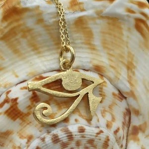 May include: A gold chain necklace with a gold pendant in the shape of the Eye of Horus, an ancient Egyptian symbol of protection.