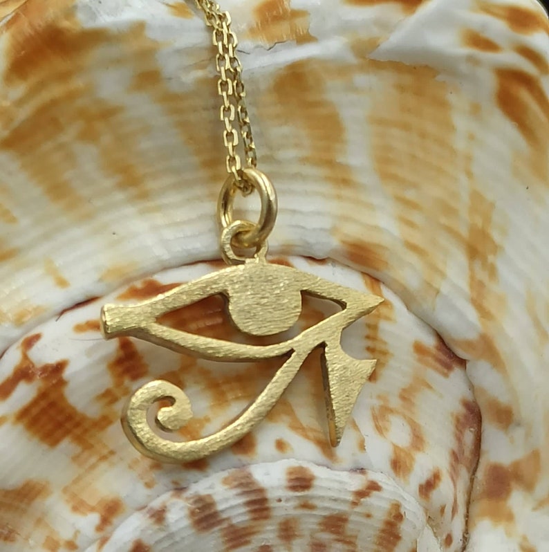 May include: A gold chain necklace with a gold pendant in the shape of the Eye of Horus, an ancient Egyptian symbol of protection.