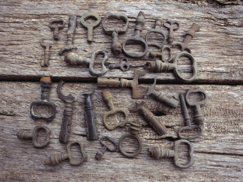 May include: A selection of antique metal keys and bottle openers, displayed on a weathered wooden surface. The items, in diverse shapes and sizes, exhibit a rustic, aged appearance with signs of wear and oxidation.