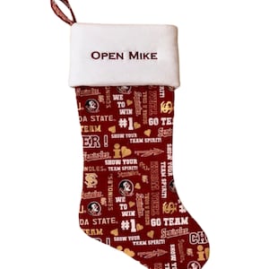 May include: A red and gold Christmas stocking with a white cuff. The cuff is personalized with the name "OPEN MIKE". The stocking is decorated with a repeating pattern of the Florida State Seminoles logo, the words "Seminoles", "Go Team", and other team-related phrases.