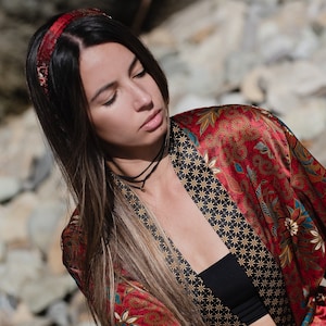 May include: A woman with long brown hair wearing a red and black patterned silk robe with a black choker necklace.