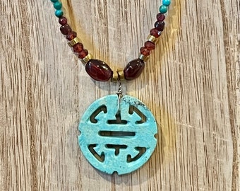 May include: A turquoise blue pendant necklace with a carved symbol, accented with maroon and gold beads.