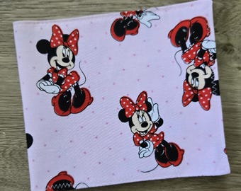 May include: A square fabric piece featuring a light pink background with a repeating pattern of Minnie Mouse wearing a red polka-dot dress and bow. The fabric is decorated with small, scattered pink dots throughout the design, creating a consistent visual motif across the entire surface of the textile material.