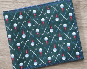 May include: A square fabric coaster featuring a dark green background with a repeating pattern of white golf balls on red tees and crossed golf clubs in white and blue. The edges are finished with a blue zigzag stitch along the entire perimeter.