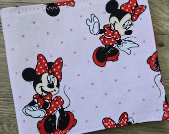May include: A square fabric item featuring a light pink background with small dark pink polka dots and a repeating pattern of Minnie Mouse. The character is depicted wearing a red dress with white polka dots and a matching red bow on her head.