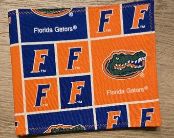 May include: A square fabric item featuring a repeating pattern of the Florida Gators logo, the letter F, and the text Florida Gators. The design uses a grid layout with alternating blocks of bright orange and royal blue, finished with a stitched edge.