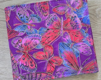May include: A square, fabric item with a vibrant purple background, adorned with a repeating pattern of colorful butterflies. The butterflies feature shades of pink, red, blue, and gold, creating a striking visual contrast.