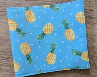 May include: A square fabric coaster featuring a light blue background with a repeating pattern of yellow pineapples and small white polka dots. The edges of the coaster are finished with a decorative zigzag stitch in a matching blue thread.