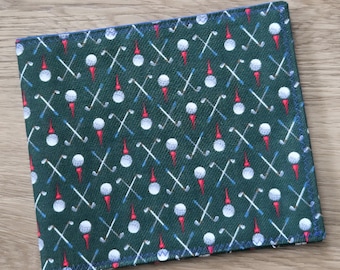 May include: A square fabric pocket square in dark green featuring a repeating pattern of white golf balls on red tees and crossed silver golf clubs with blue grips. The edges are finished with a dark blue stitched border on all four sides.